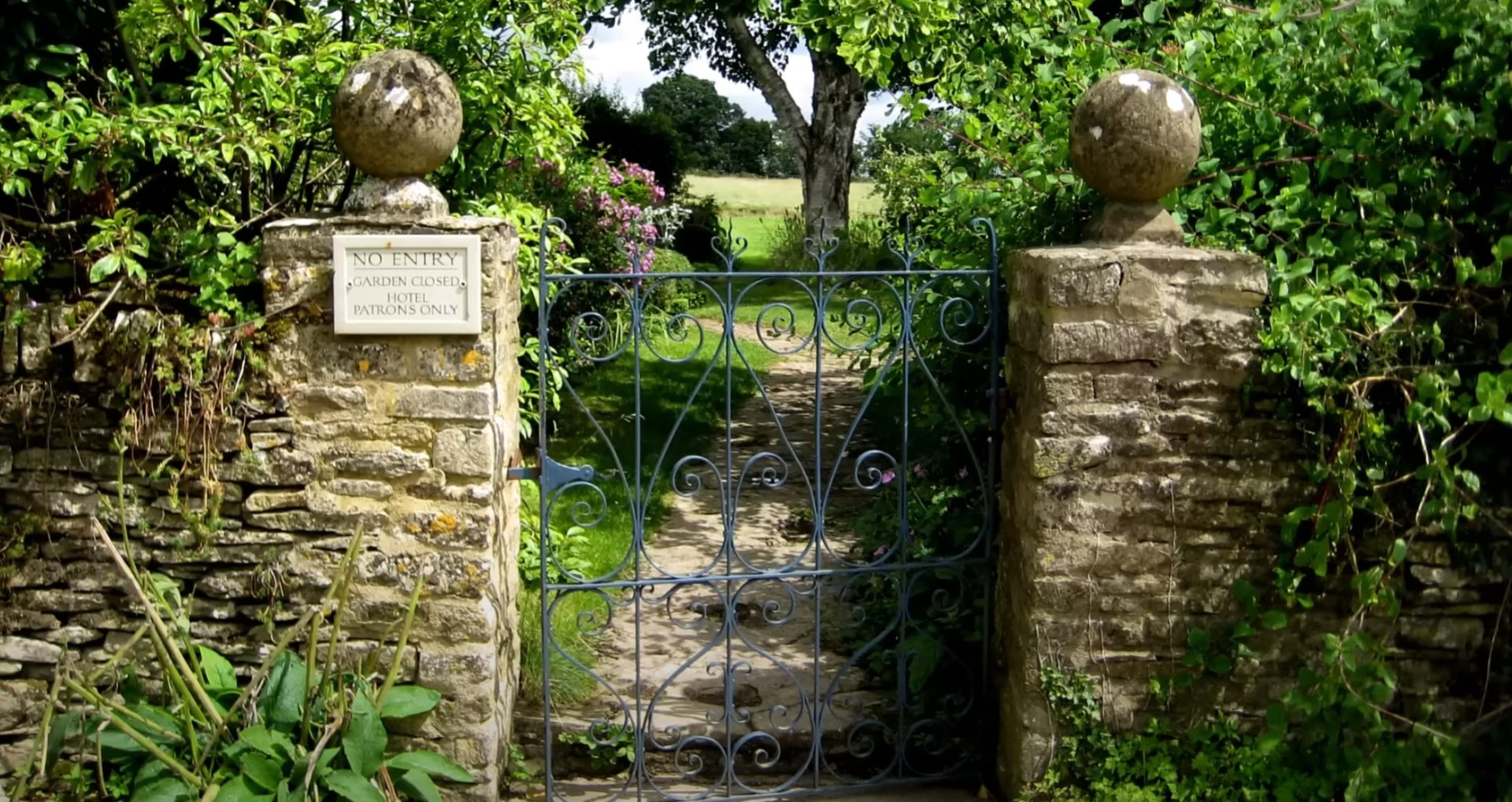 Professional hardscaping installation with natural stone pillars and ornamental plantings Elegant stone entrance with decorative iron gates and mature landscaping