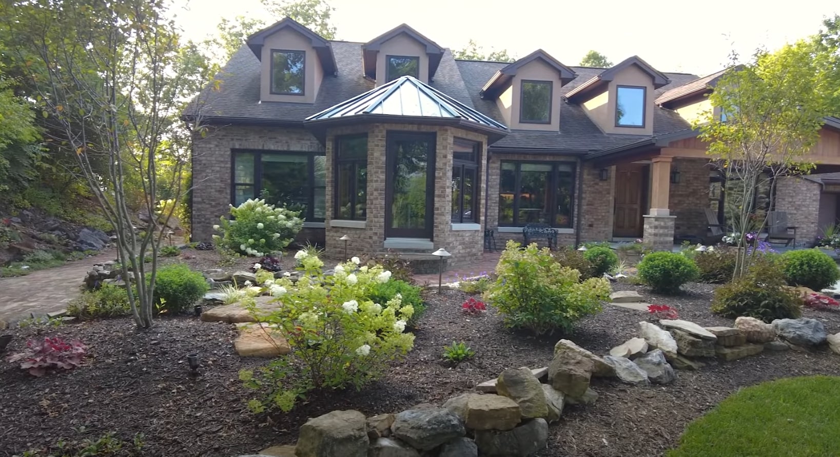 High-end residential landscaping with natural stone hardscaping and professional shrub care Luxury home front yard with natural stone landscaping, decorative plantings, and mature shrubs